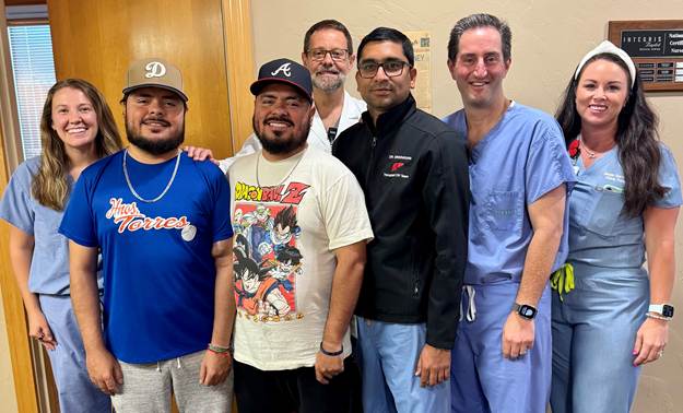 Two twins, one in white and one in blue, posing with the transplant staff.