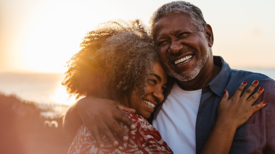 A couple smiling and hugging on the beach with a sunset in the background