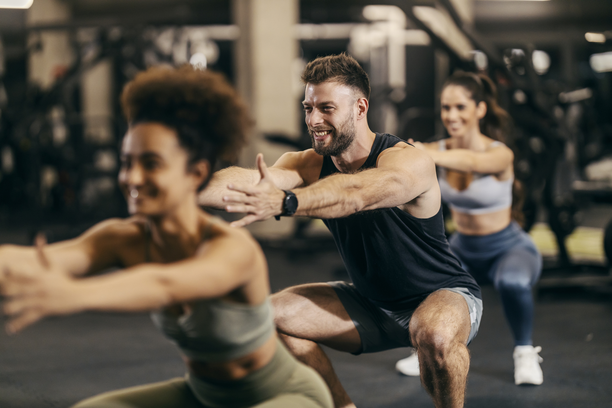 People in a gym squat with arms extended