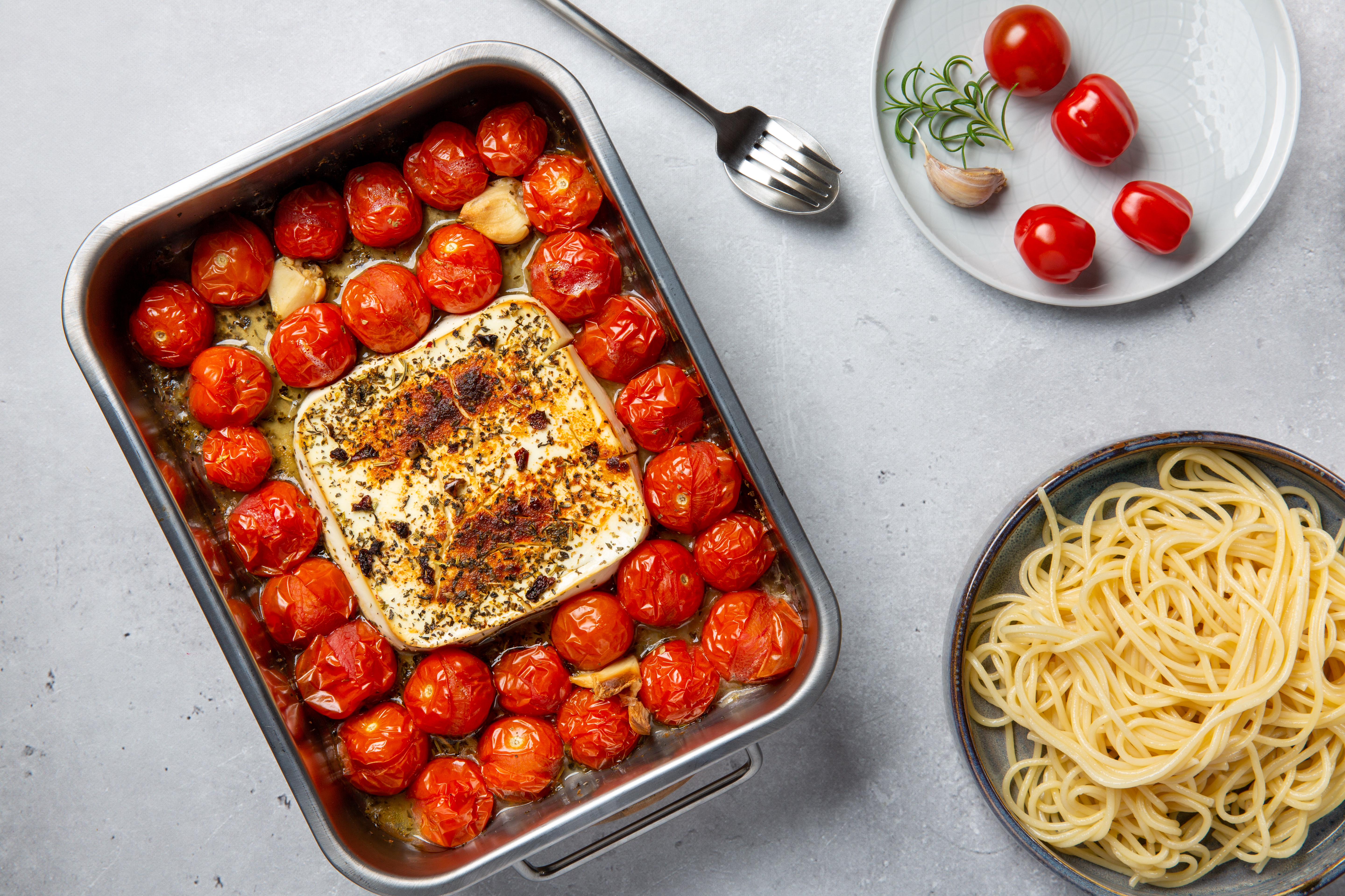 baked feta in a pan next to a plate and a pot of cooked pasta