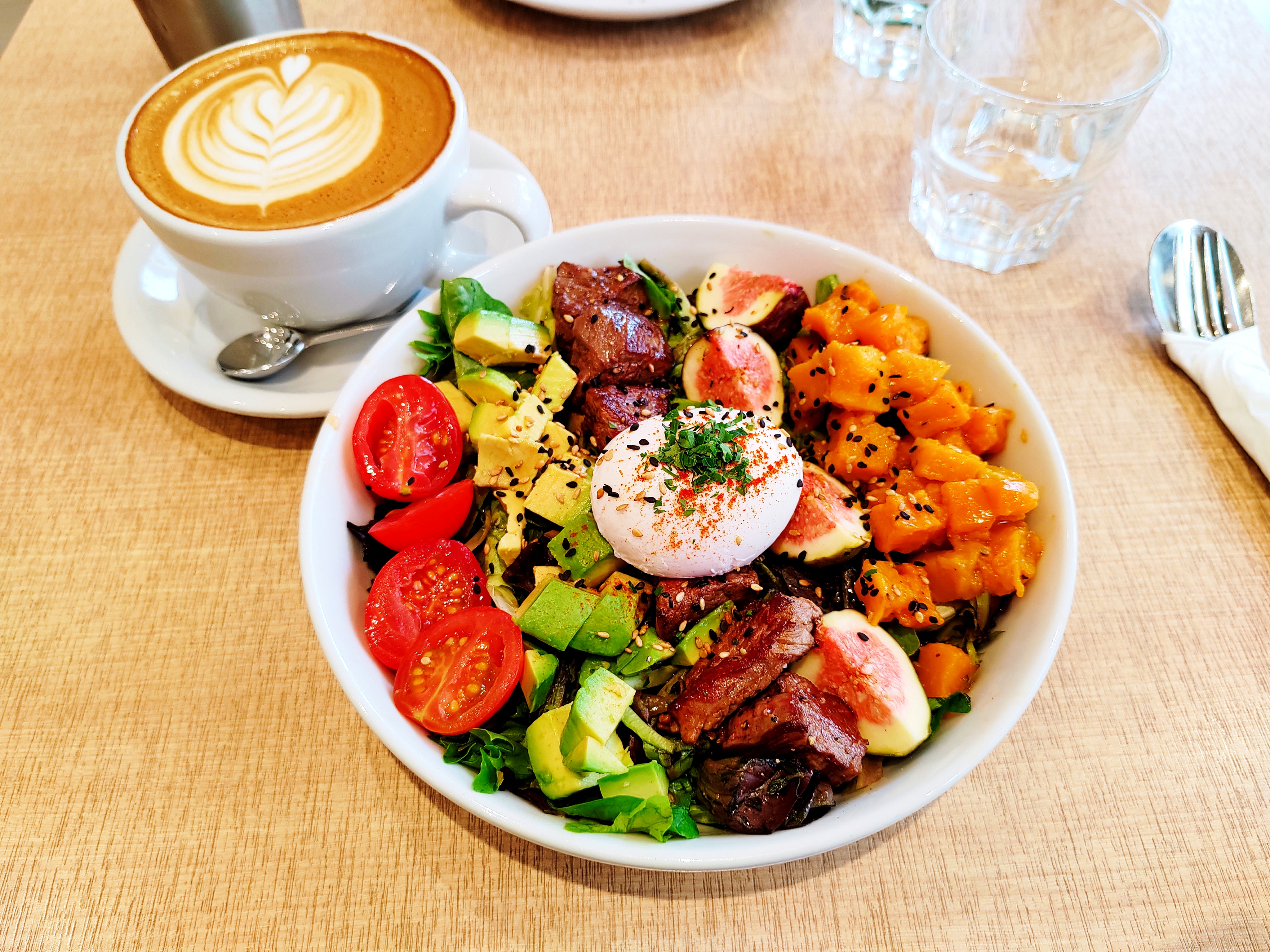 Beef, avocado and sweet potato in a white bowl, with tomatoes and a poached egg added
