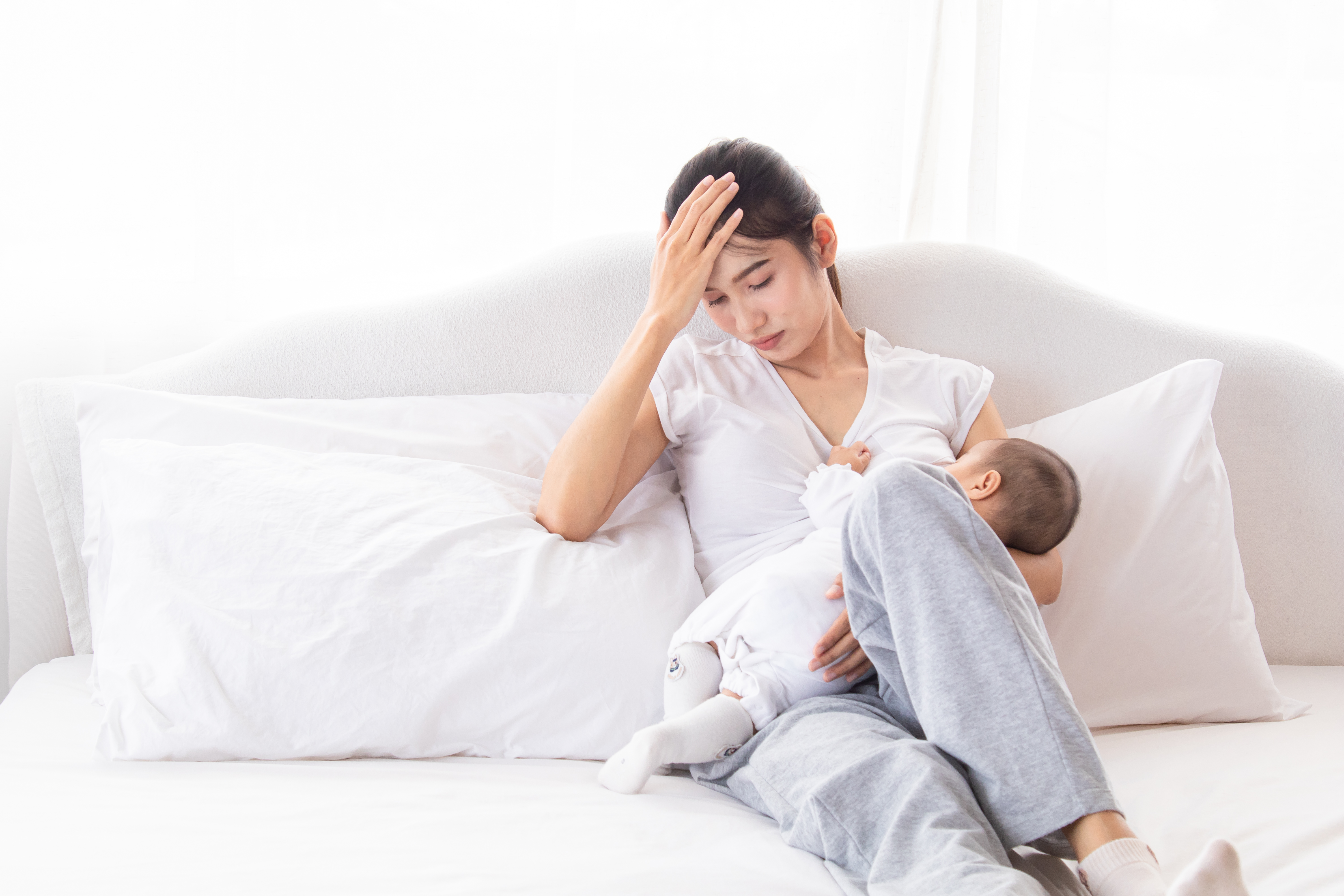 a woman holds her head in her hand while her baby latches