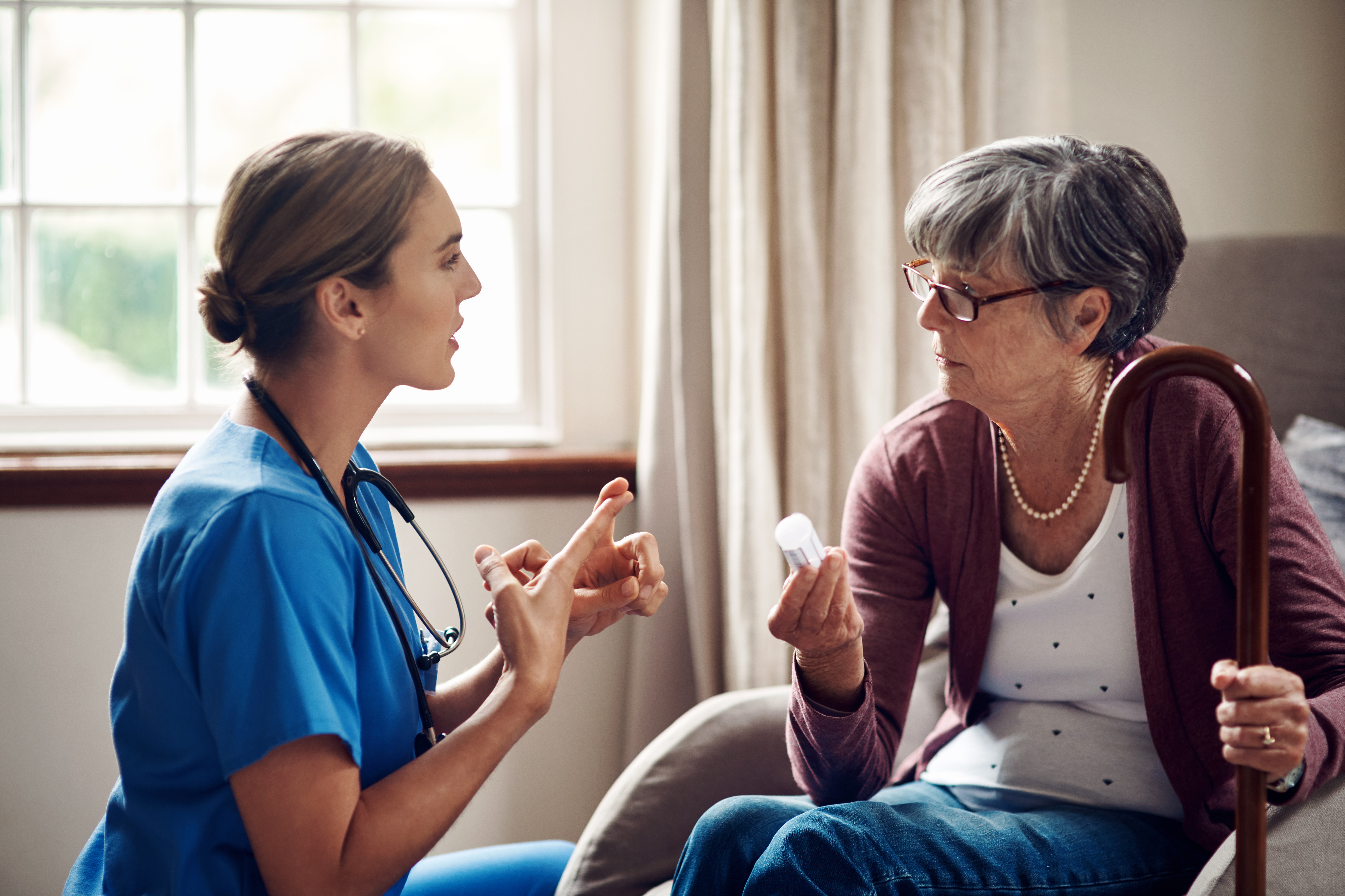 A health care worker in scrubs explains medications to an older patient 