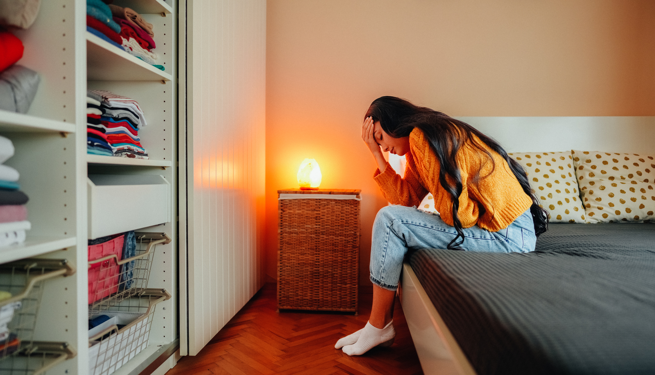 A woman sits hunched on her bed in pain