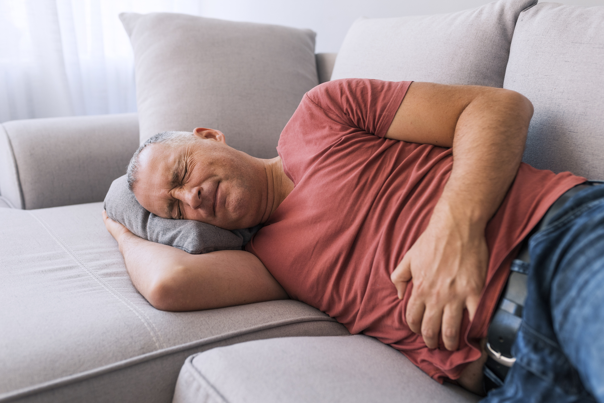 A man lying in pain on the couch while grabbing his stomach