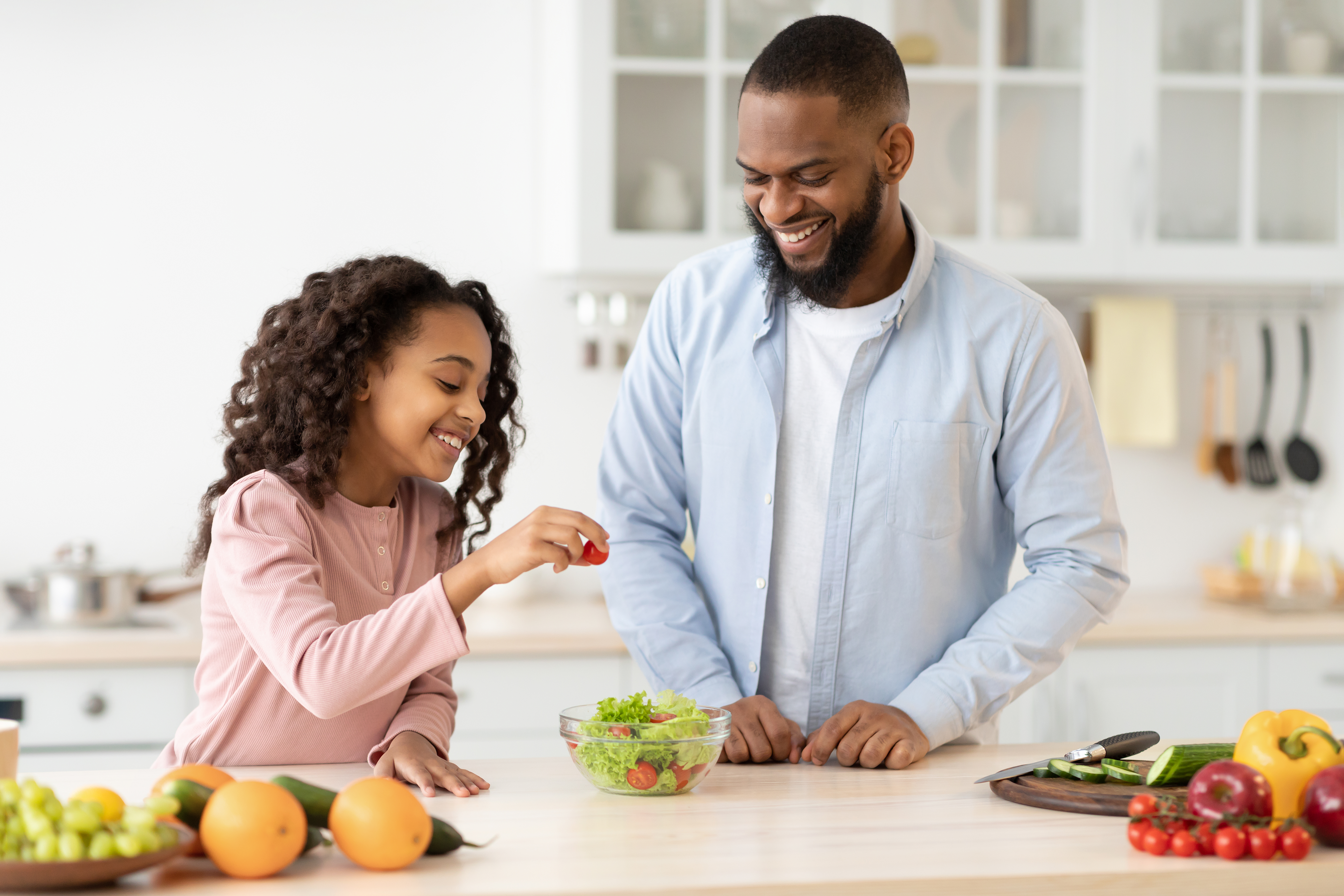 A father and daughter make a salad together in the kitchen