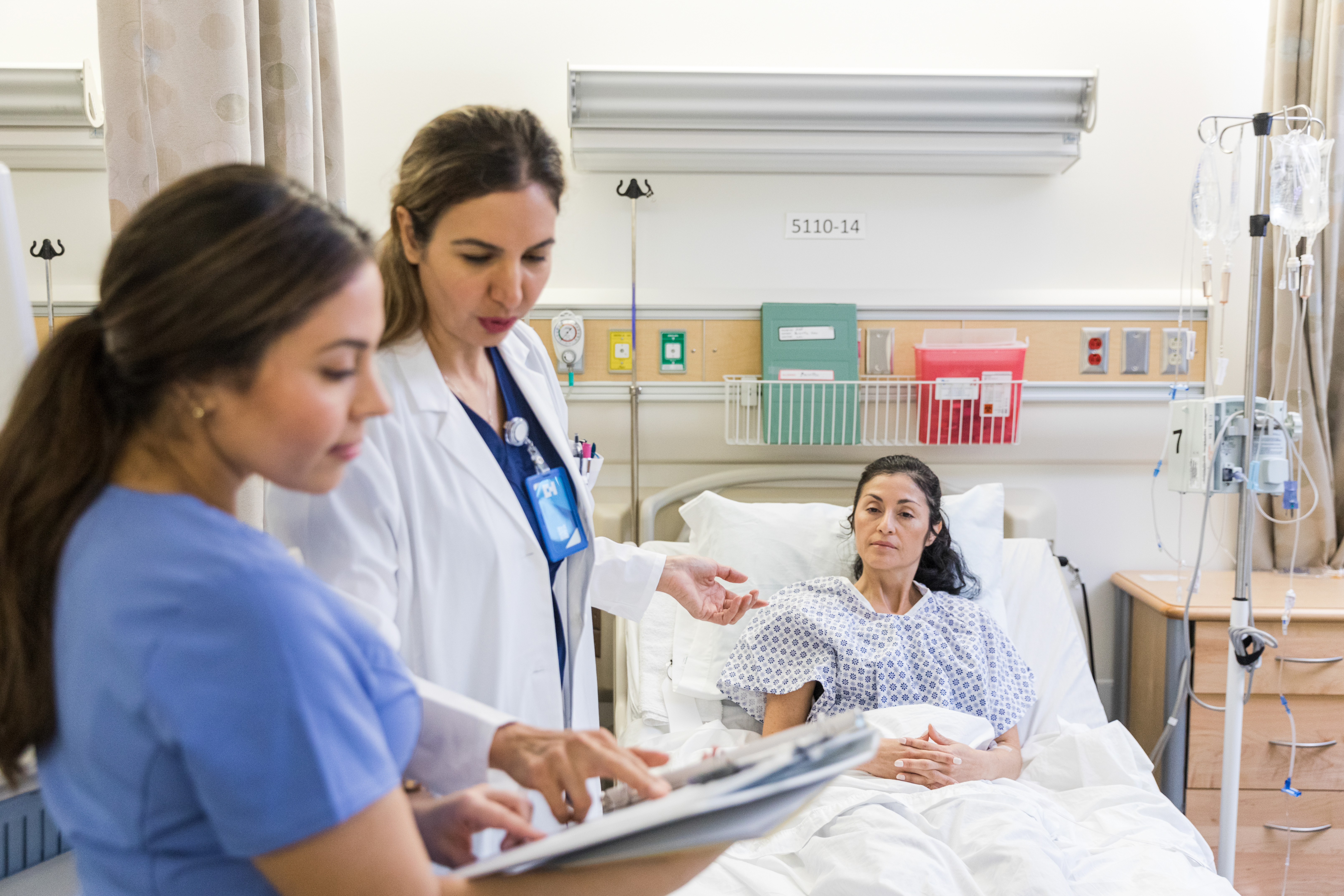 A doctor and nurse discuss with a female patient lying in a hospital bed