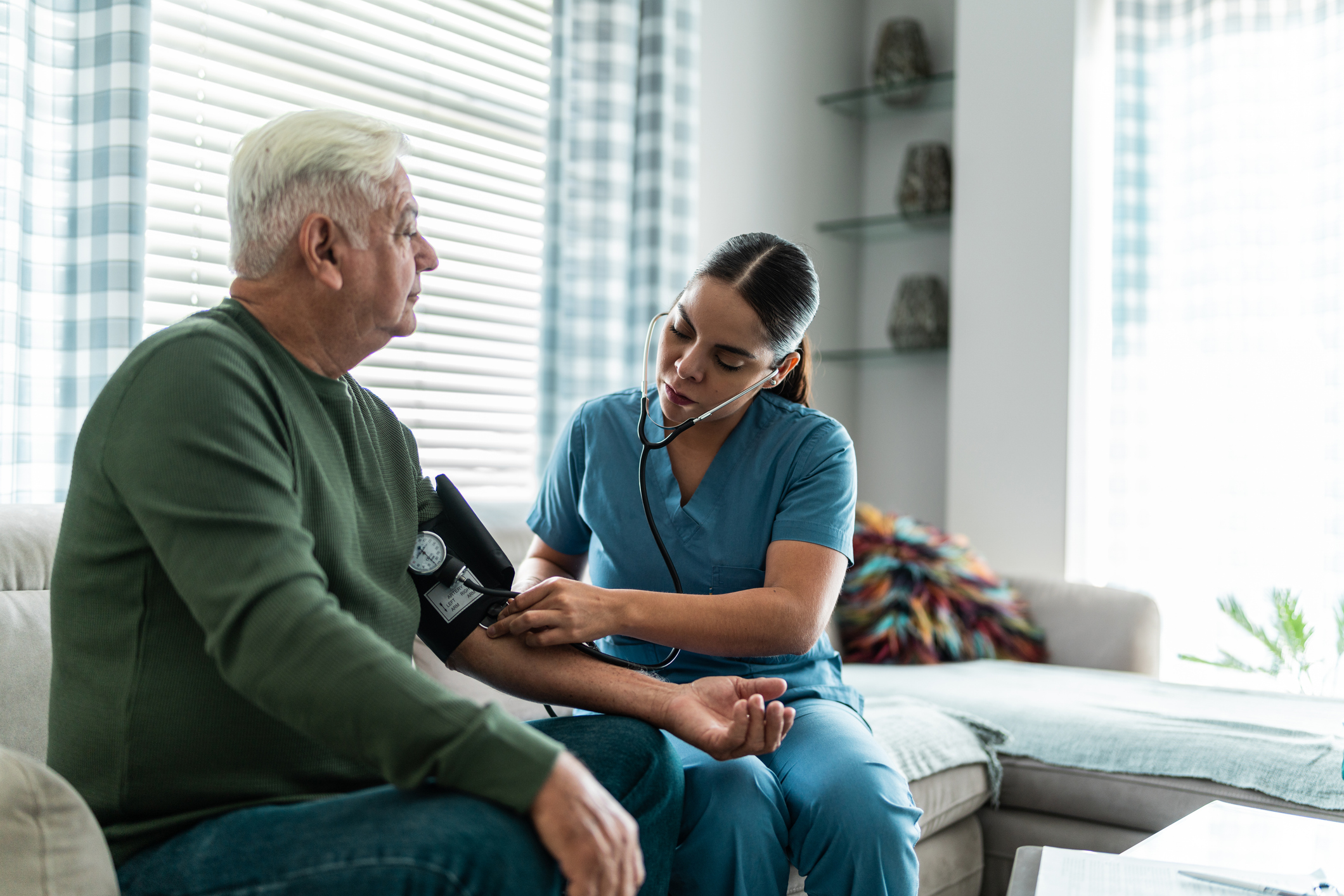 An older man gets his blood pressure checked by a nurse in scrubs
