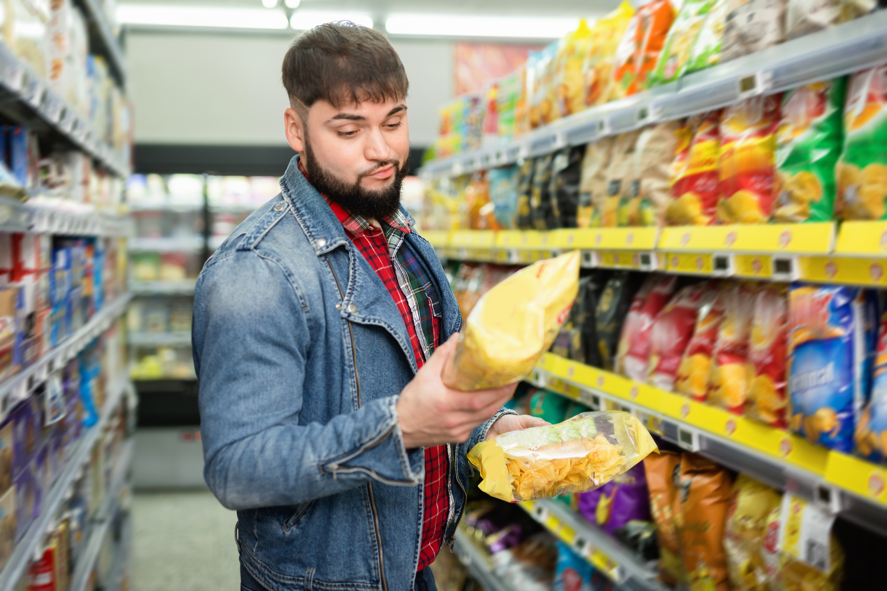 a man in a grocery store reads the ingredients on a bag of chips
