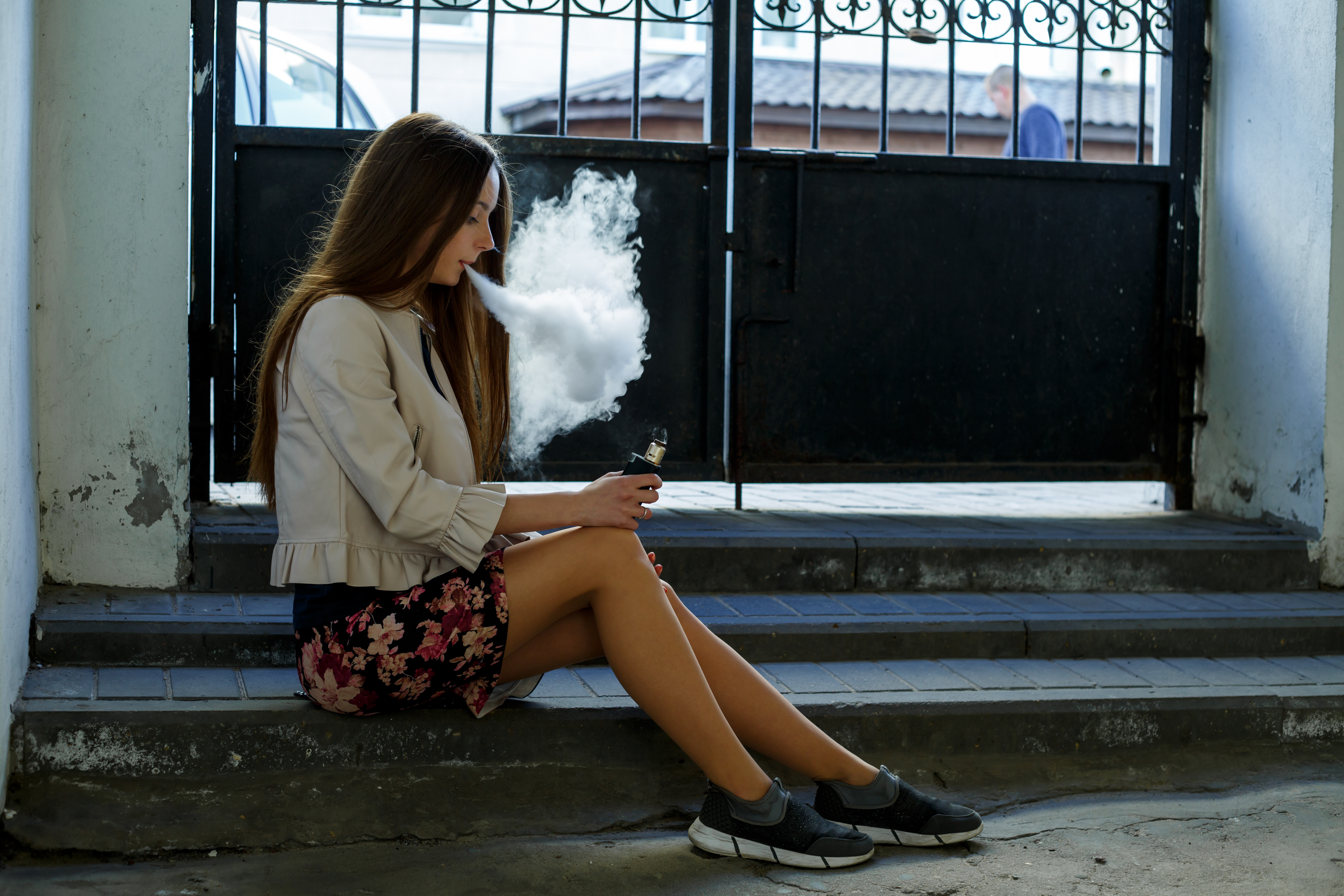 a teen girl sits and vapes, blowing out a cloud of vapor