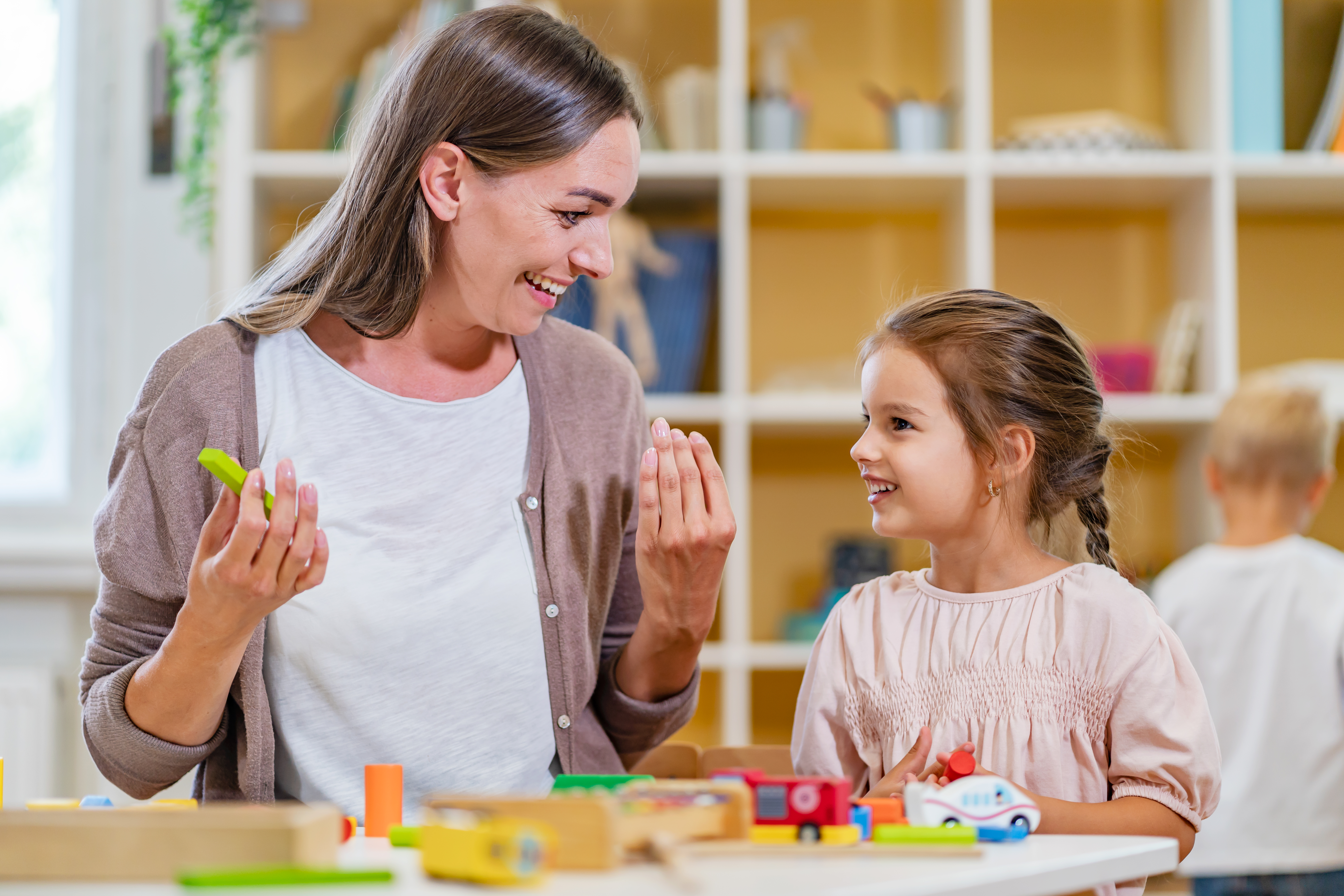 a woman and young child play at a table with toys