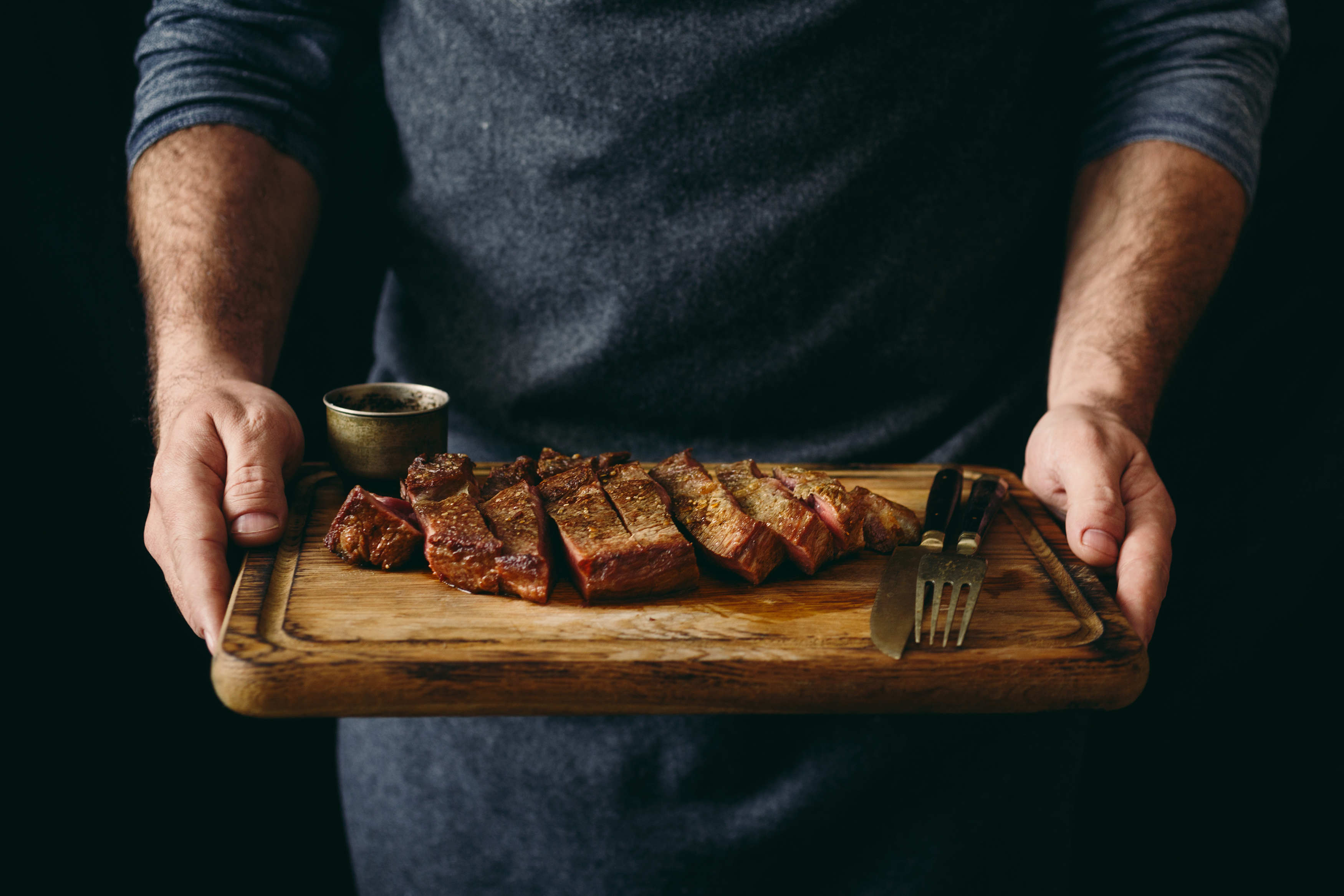 Man holding juicy grilled beef steak with spices on cutting board