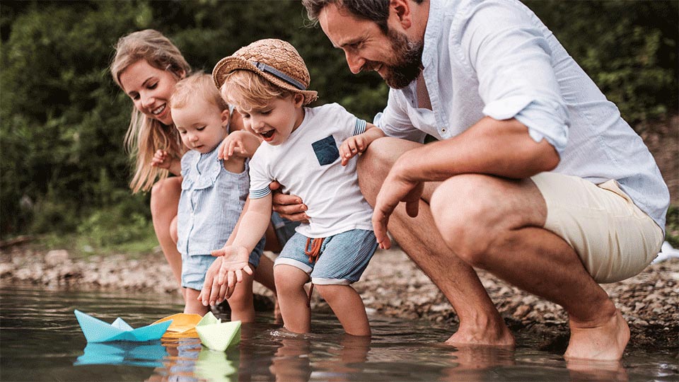 family playing with paper boats in stream